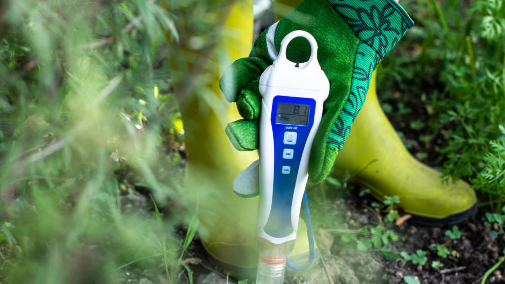 A person wearing gardening gloves holds a soil pH meter in a garden